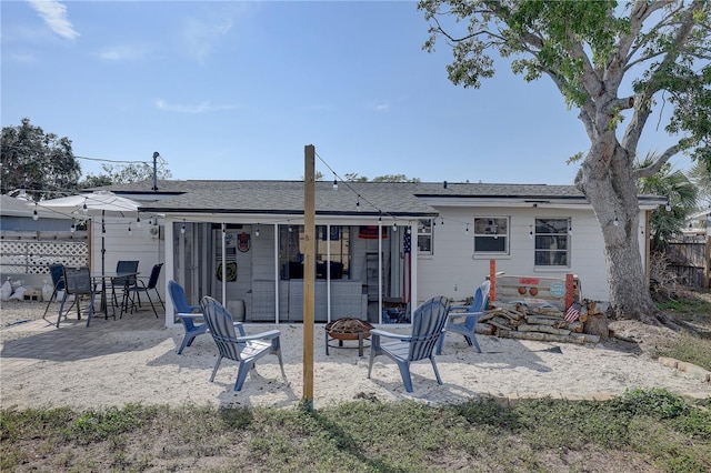 rear view of property featuring a patio area, fence, a fire pit, and roof with shingles