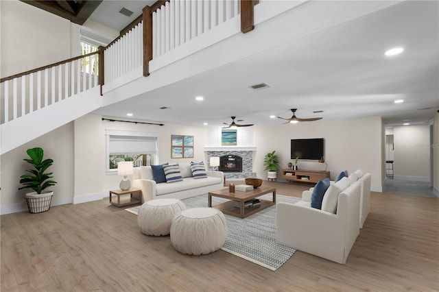 living room featuring ceiling fan, a fireplace, light hardwood / wood-style flooring, and a high ceiling