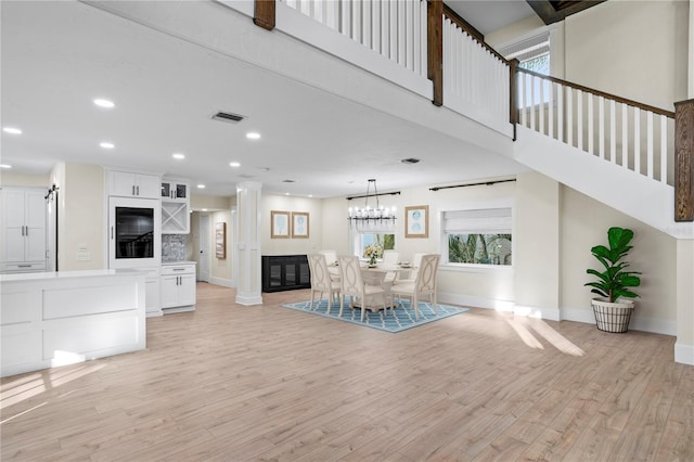 unfurnished dining area featuring a high ceiling, a barn door, light hardwood / wood-style floors, and ornate columns