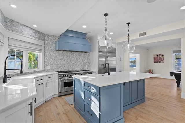 kitchen with sink, high end appliances, white cabinets, a center island with sink, and custom exhaust hood