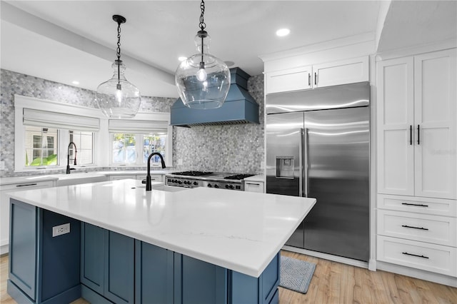 kitchen with decorative light fixtures, an island with sink, sink, white cabinets, and stainless steel built in fridge