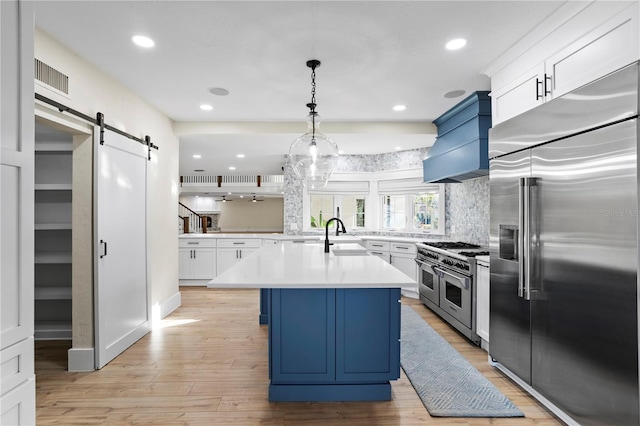 kitchen with premium range hood, high end appliances, an island with sink, a barn door, and white cabinets