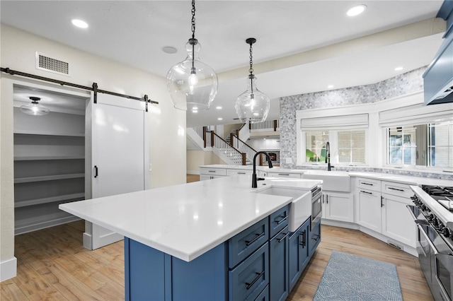 kitchen featuring blue cabinets, an island with sink, a barn door, and sink