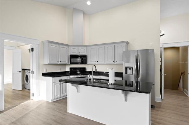 kitchen with washer / clothes dryer, a breakfast bar, a high ceiling, and range with electric stovetop