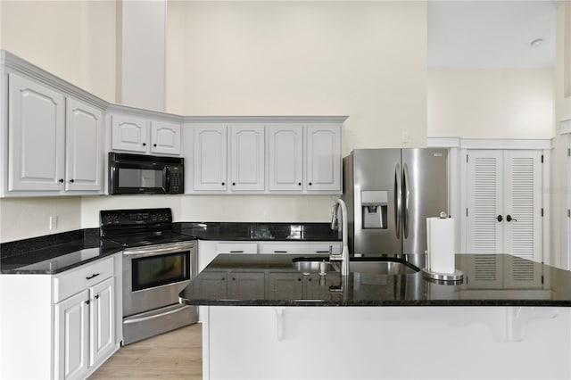 kitchen featuring sink, dark stone countertops, stainless steel appliances, light hardwood / wood-style floors, and white cabinets