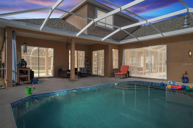 pool at dusk featuring ceiling fan, glass enclosure, and a patio area