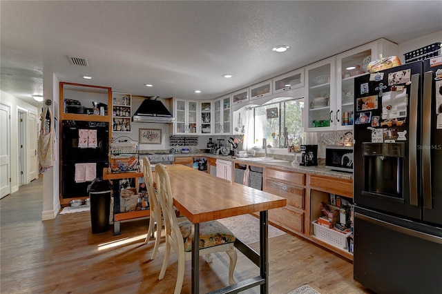 kitchen with sink, white cabinets, wall chimney exhaust hood, black appliances, and light hardwood / wood-style flooring