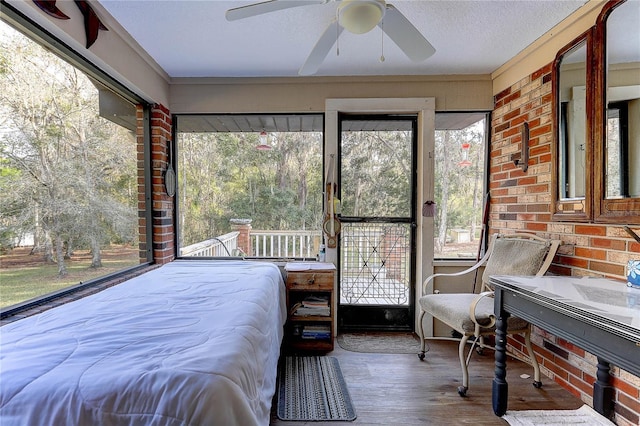 bedroom with ceiling fan, brick wall, wood-type flooring, and a textured ceiling