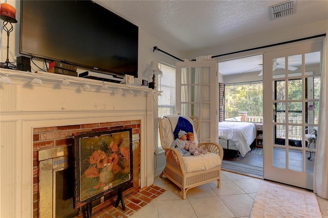 sitting room featuring a brick fireplace, light tile patterned floors, a textured ceiling, and ceiling fan