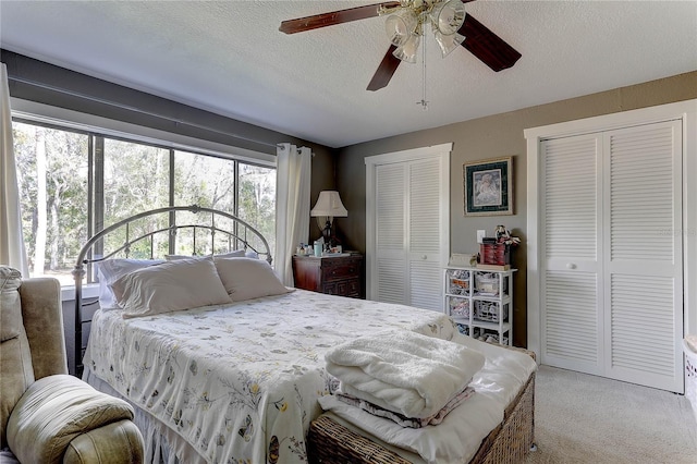 bedroom with ceiling fan, a textured ceiling, light carpet, and two closets