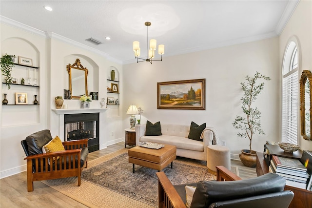 living room with crown molding, built in shelves, a notable chandelier, and light hardwood / wood-style flooring