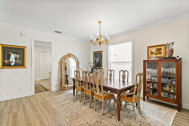 dining room featuring a notable chandelier, ornamental molding, a textured ceiling, and light wood-type flooring