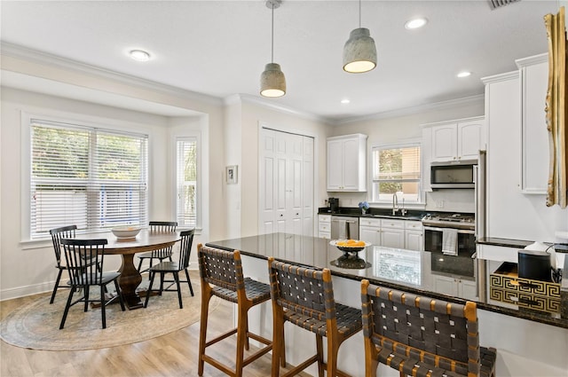 kitchen with decorative light fixtures, white cabinetry, sink, stainless steel appliances, and light hardwood / wood-style flooring