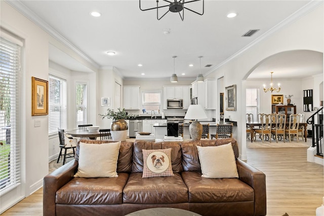 living room featuring a notable chandelier, a wealth of natural light, light hardwood / wood-style floors, and ornamental molding