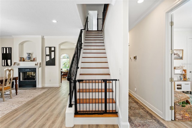 staircase featuring crown molding, hardwood / wood-style floors, and a multi sided fireplace