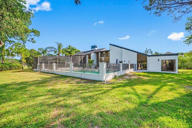 rear view of house with a fenced in pool, a lanai, and a lawn