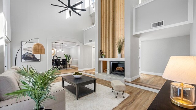 living room with ceiling fan, a towering ceiling, and hardwood / wood-style floors