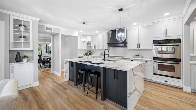 kitchen with white cabinetry, wall chimney range hood, sink, and stainless steel double oven