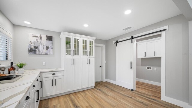 interior space featuring a barn door, light stone countertops, light hardwood / wood-style flooring, and white cabinets