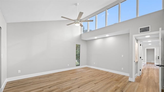 unfurnished living room with ceiling fan, a towering ceiling, and light wood-type flooring