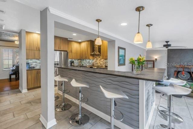 kitchen featuring pendant lighting, wall chimney exhaust hood, stainless steel fridge with ice dispenser, and decorative backsplash