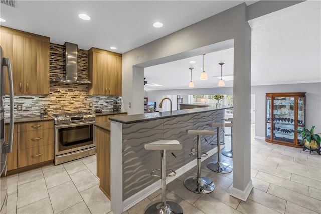 kitchen featuring gas stove, decorative light fixtures, a breakfast bar area, and wall chimney exhaust hood