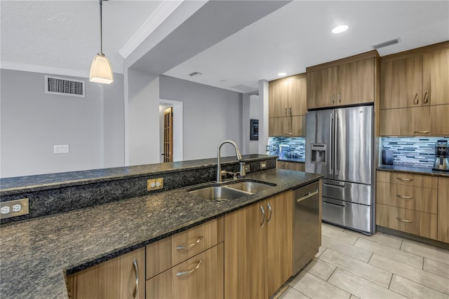 kitchen featuring sink, dark stone countertops, decorative backsplash, hanging light fixtures, and stainless steel appliances