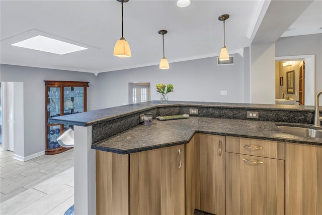 kitchen with a skylight, sink, pendant lighting, and dark stone counters