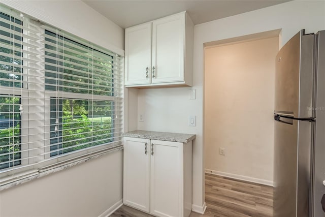 kitchen featuring white cabinets, stainless steel fridge, light stone counters, and light hardwood / wood-style flooring