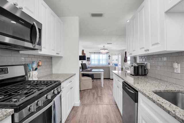 kitchen featuring appliances with stainless steel finishes, white cabinetry, decorative backsplash, light hardwood / wood-style floors, and light stone countertops