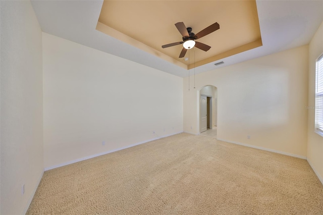 spare room featuring light colored carpet, a raised ceiling, and ceiling fan