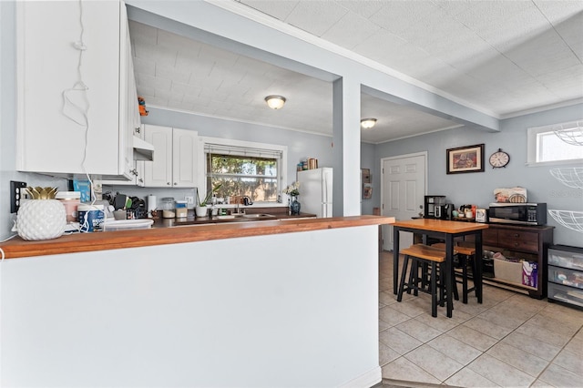 kitchen featuring light tile patterned flooring, butcher block counters, white refrigerator, ornamental molding, and white cabinets