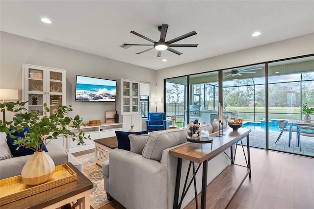 living room with ceiling fan, a textured ceiling, and light hardwood / wood-style floors