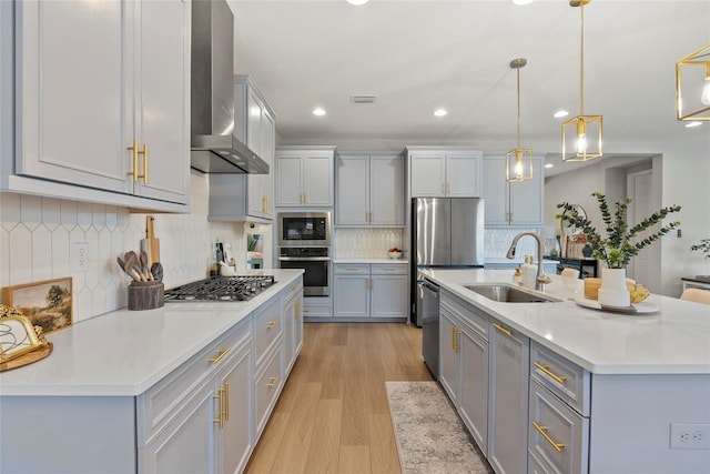 kitchen featuring sink, a center island with sink, hanging light fixtures, appliances with stainless steel finishes, and wall chimney range hood