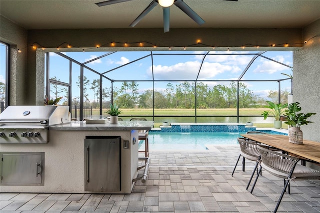 view of pool with exterior kitchen, pool water feature, grilling area, and glass enclosure