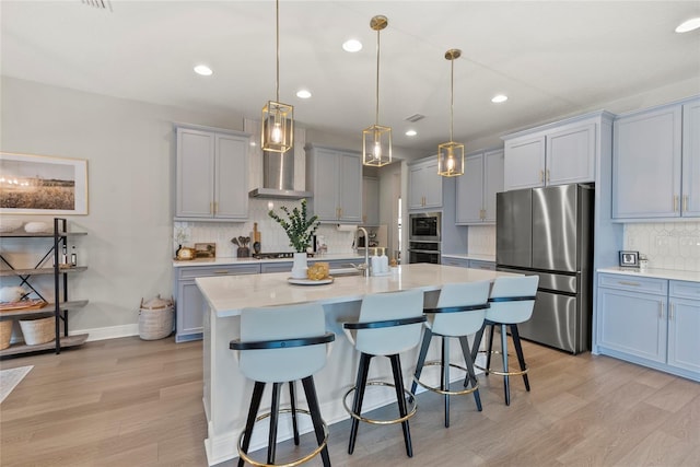 kitchen with appliances with stainless steel finishes, pendant lighting, sink, wall chimney range hood, and a center island with sink