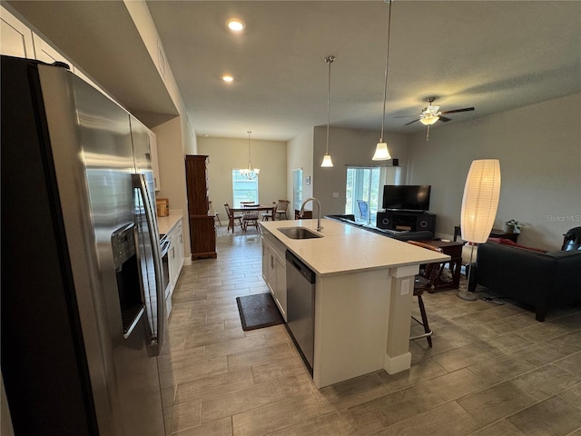 kitchen with decorative light fixtures, an island with sink, sink, white cabinets, and stainless steel appliances