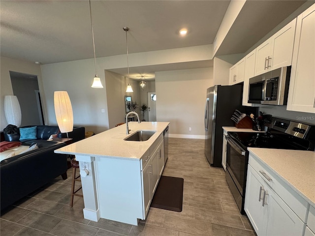 kitchen with appliances with stainless steel finishes, white cabinetry, sink, hanging light fixtures, and a center island with sink