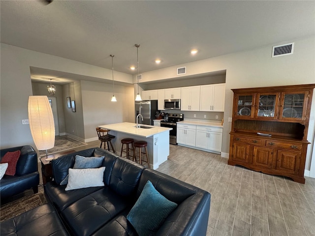 kitchen with sink, white cabinetry, hanging light fixtures, stainless steel appliances, and an island with sink