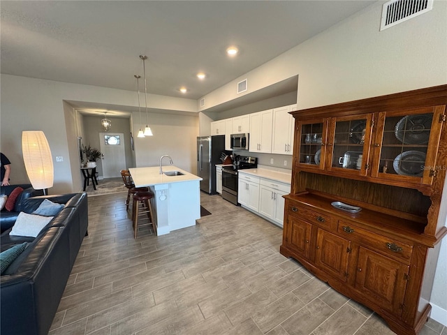 kitchen with a kitchen bar, sink, appliances with stainless steel finishes, an island with sink, and pendant lighting