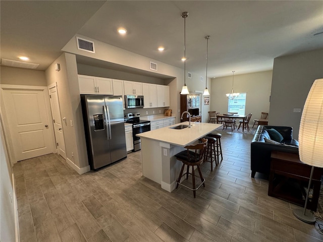 kitchen with sink, a breakfast bar, appliances with stainless steel finishes, white cabinets, and a center island with sink