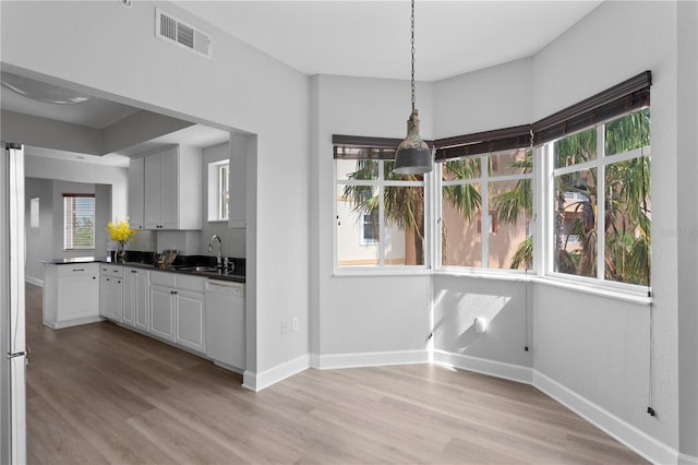 kitchen with white dishwasher, sink, decorative light fixtures, and light wood-type flooring