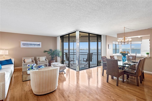 living room featuring floor to ceiling windows, a water view, a chandelier, a textured ceiling, and light hardwood / wood-style floors