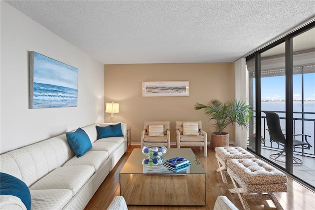 living room featuring a water view, hardwood / wood-style floors, a textured ceiling, and a wall of windows