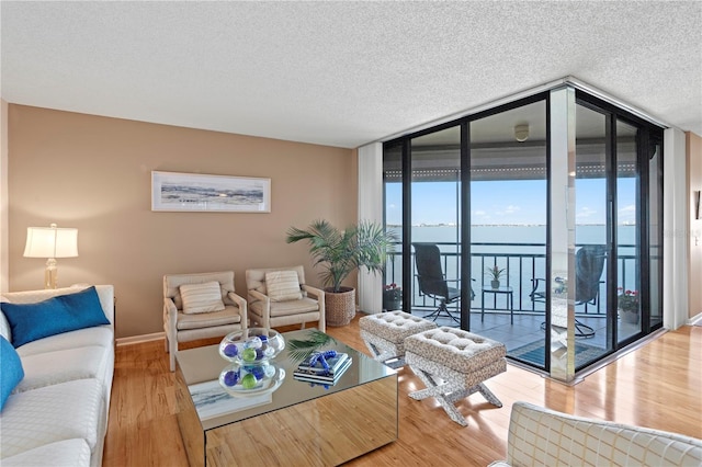 living room featuring a water view, hardwood / wood-style floors, a textured ceiling, and a wall of windows