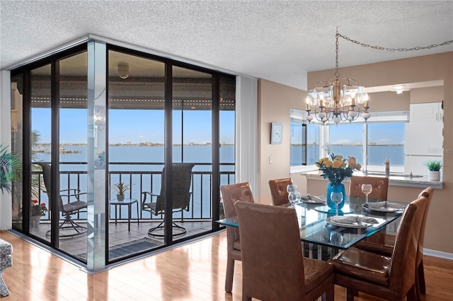 dining room featuring hardwood / wood-style flooring, a water view, expansive windows, a textured ceiling, and a chandelier