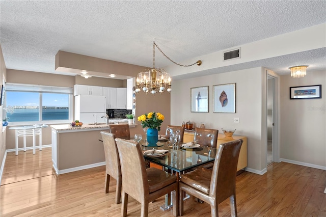 dining area featuring a water view, a notable chandelier, light hardwood / wood-style flooring, and a textured ceiling