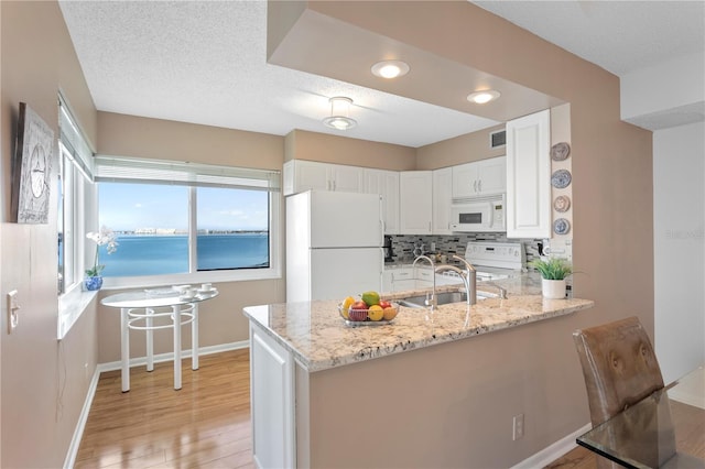 kitchen featuring light stone countertops, white cabinetry, a water view, and white appliances