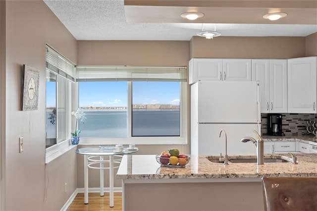 kitchen with light stone countertops, a water view, white cabinets, and white fridge