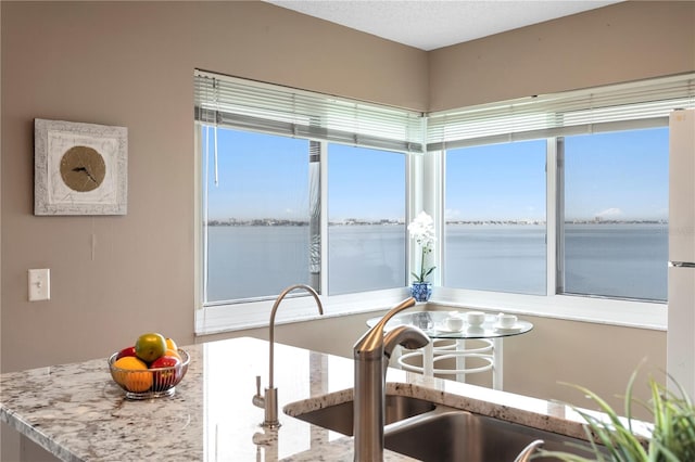 kitchen featuring a water view, sink, light stone counters, and a textured ceiling